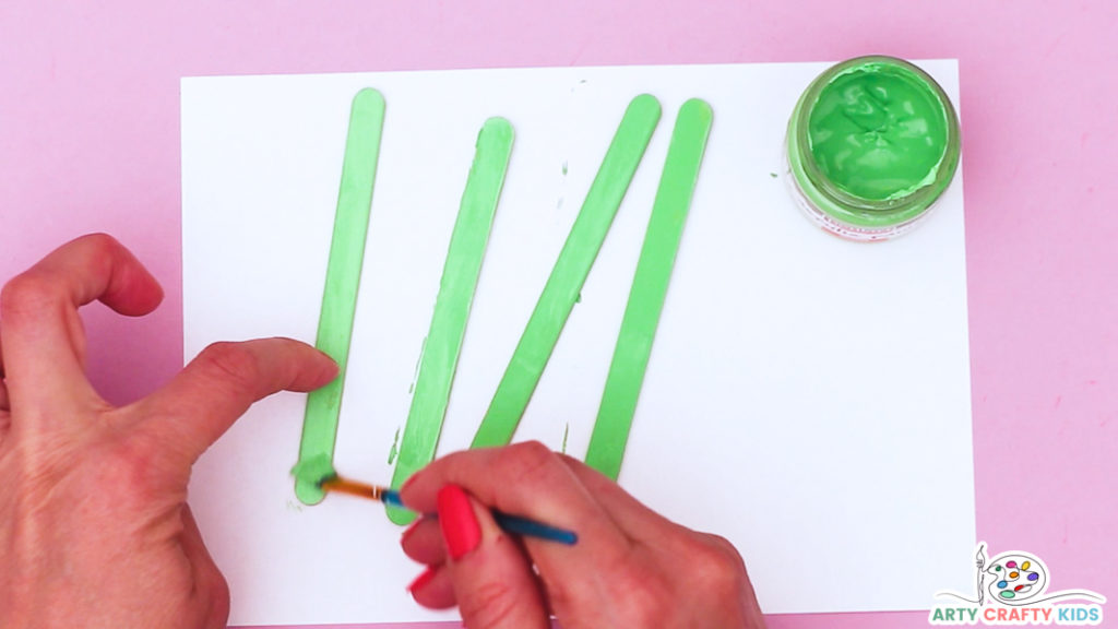 Image features a hand painting the popsicle sticks green.
