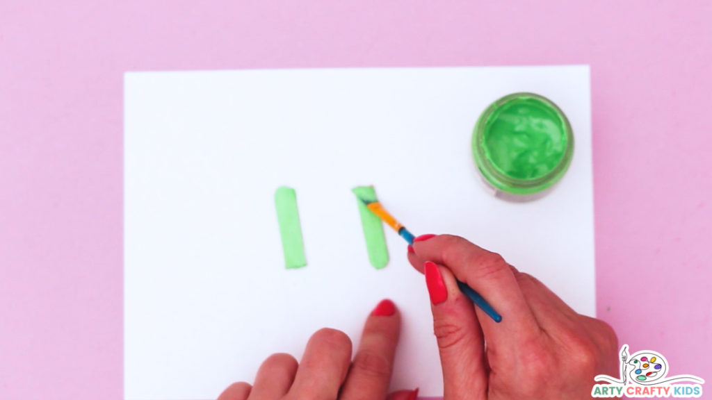 Image features a hand painting two smaller popsicle sticks green.