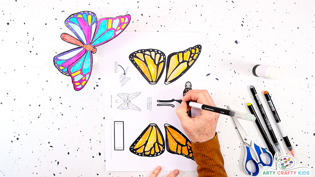 Image featuring the butterfly template colored in a Monarch butterfly pattern. A hand is finishing off the butterfly's antenna.
