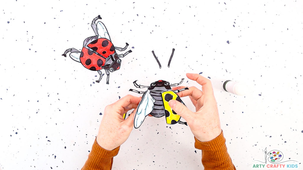 Image features a hand affixing the ladybug's outer shell on top of the ladybug.