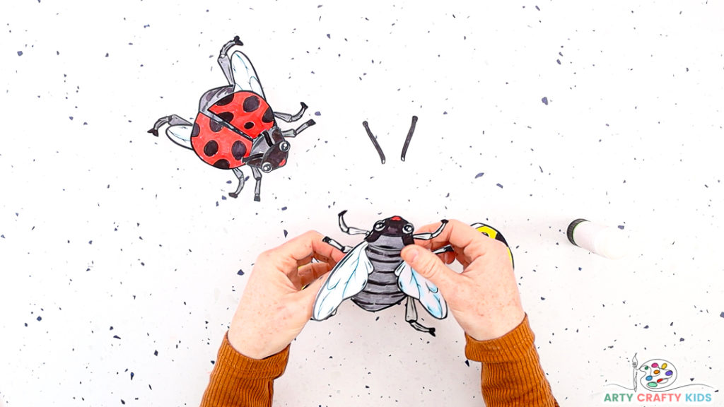 Image features a hand affixing a pair of wings to the ladybug.