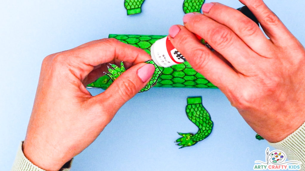 Image of a hand applying glue to a folded flap onto of one of four crocodile legs.