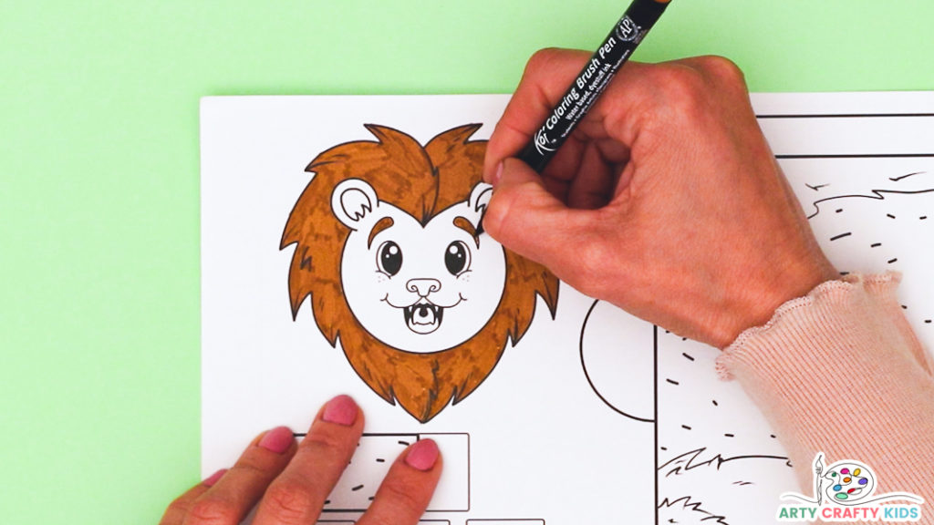 Image featuring a hand coloring in the mane and eyebrows of the lion template a brown and orange color.