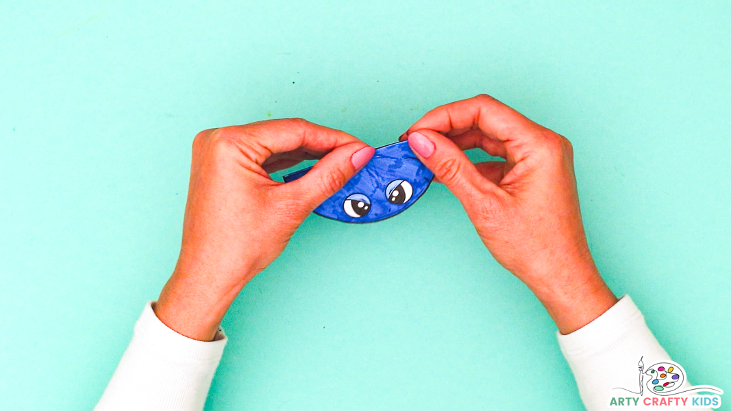 Image featuring a pair of hands folding the glue body and mouth piece in half - the eyes are on top and the shark is colored in blue.
