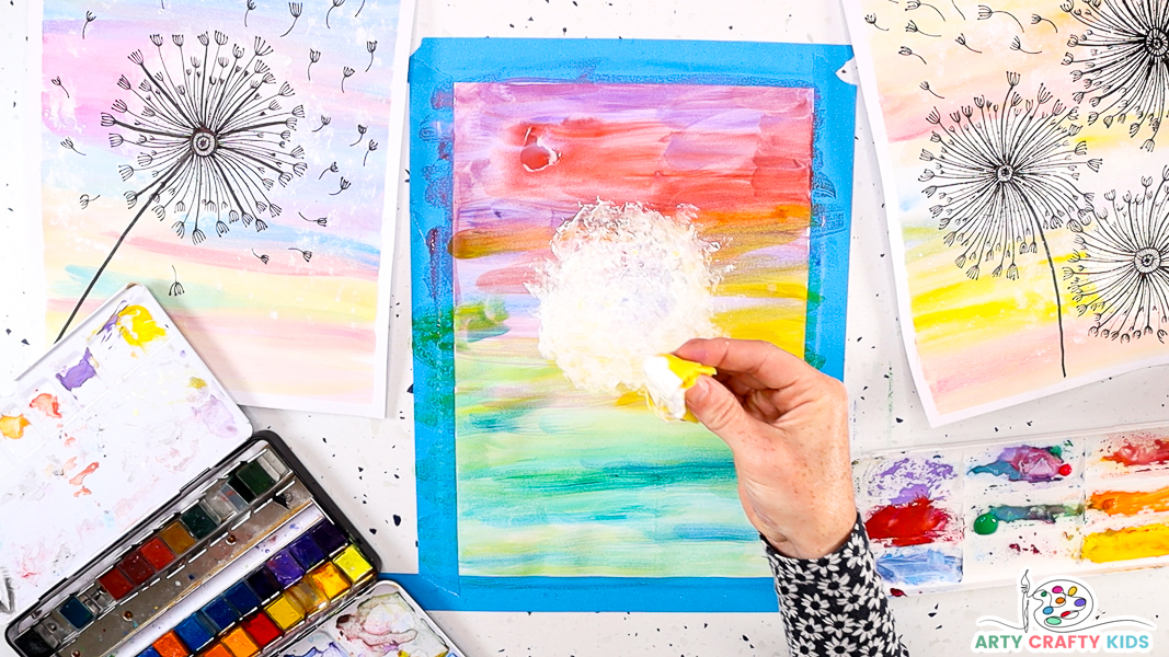 This image features a large round dandelion puff in the center of the watercolor backdrop. The hand is holding up the tissue paper to show the white paint on the bottom.