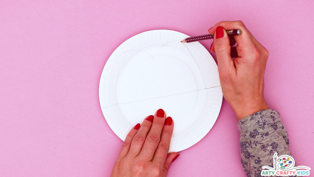 This image features a hand drawing the eyes of a crocodile onto a white paper plate.