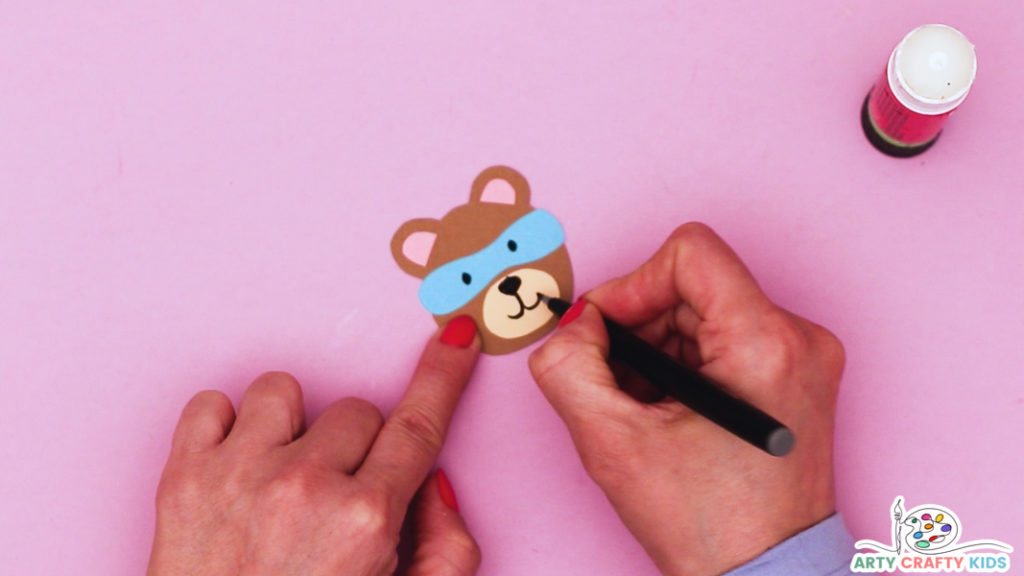 Image featuring a hand drawing a smiley face onto an assembled bear head.