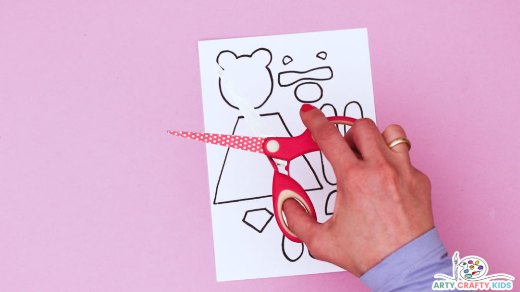 Image featuring a hand holding a pair of scissors above the paper roll superhero bear craft template.