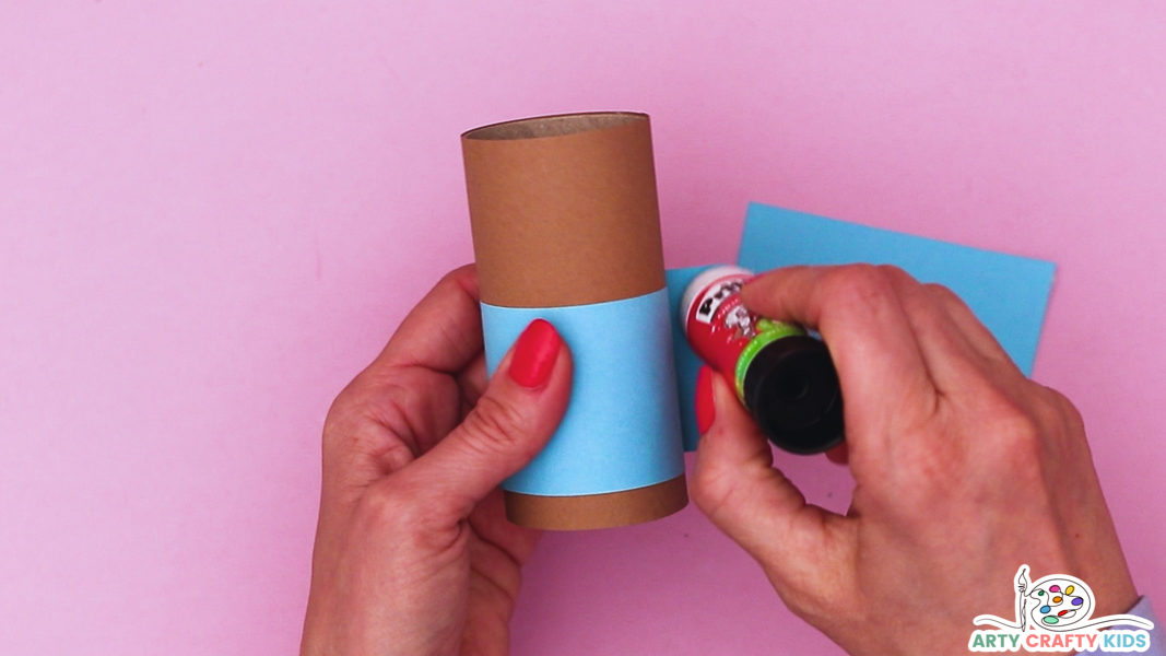 Image featuring a hand glueing a strip of blue paper around the paper roll strip.