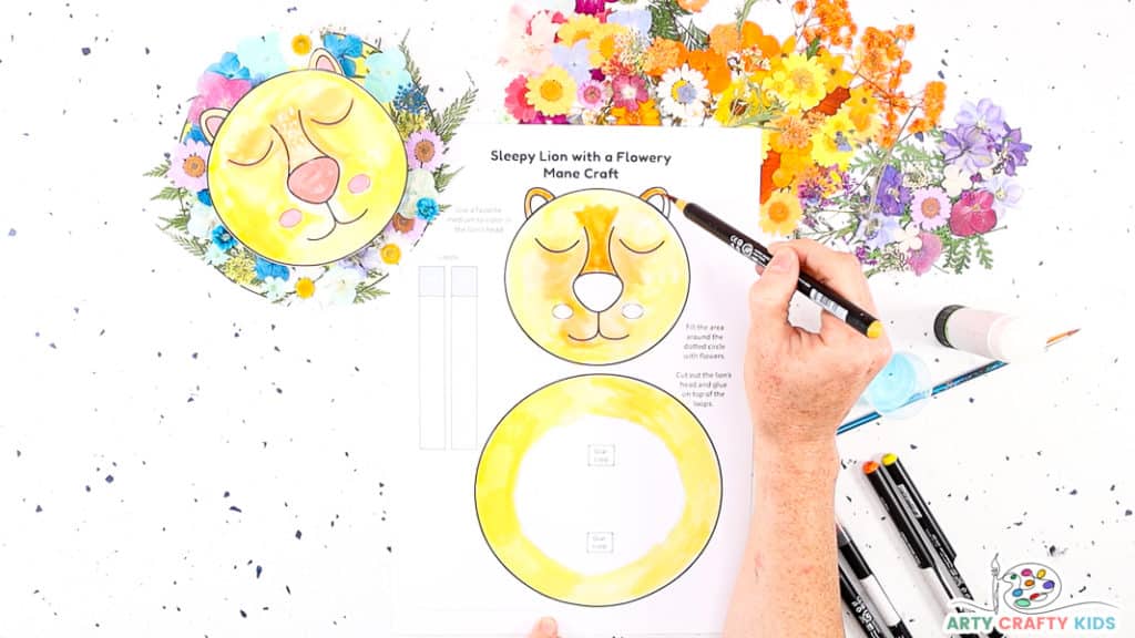 Image featuring a hand creativity coloring in the lion's head in different shades of yellow and orange. 