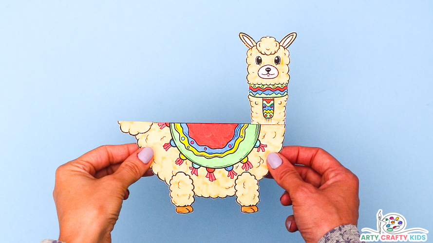 A pair of hand holding a completed 3D Paper Llama Craft | A Llama Coloring Craft - the body is beige with a colorful neck scarf and rug hanging over the body.