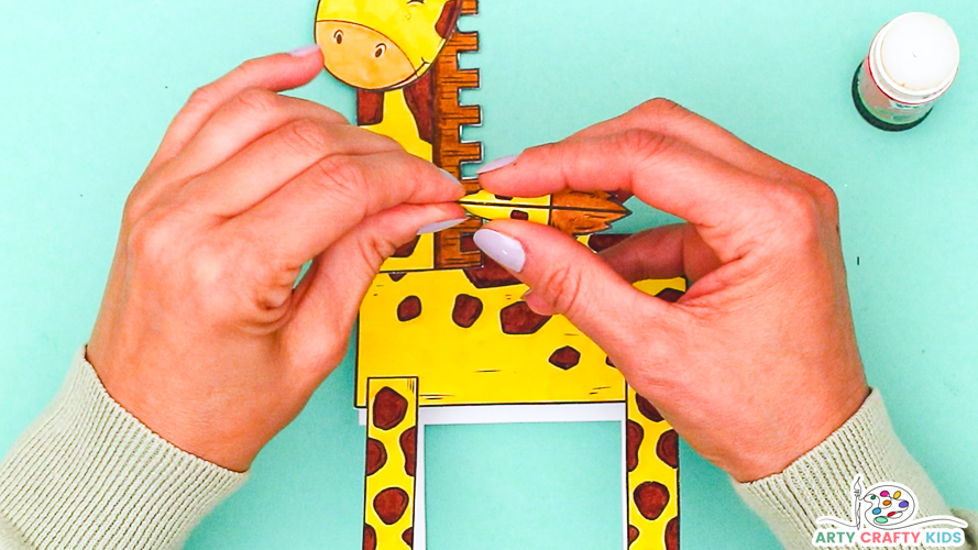 Image featuring hands folding the tail element in half and affixing to the giraffe's body.