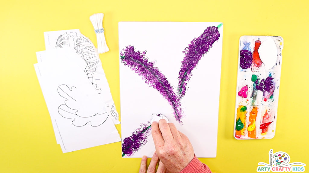 Image of a hand completing the 3rd stem - all are filled with purple prints, shaped like a buddiea flowers - these form the basis of the butterfly bush.