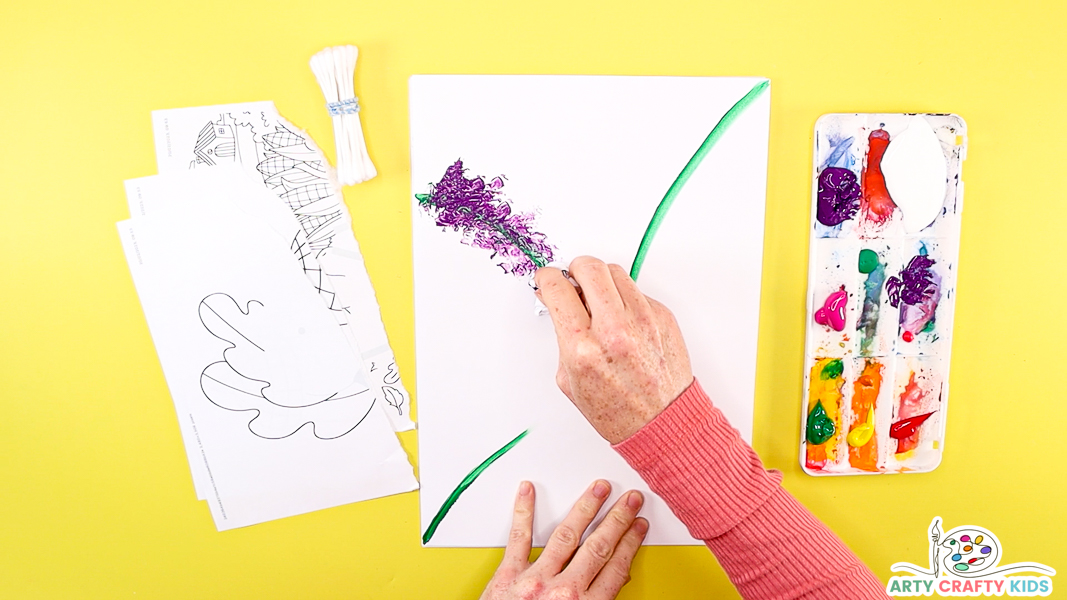 Image of a hand using the scrunched up paper to print purple paint along one of the green stems. 
