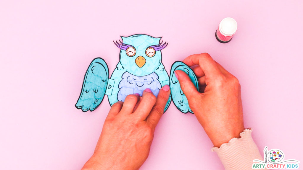 Image of a hand glueing the wings onto the body of the owl.