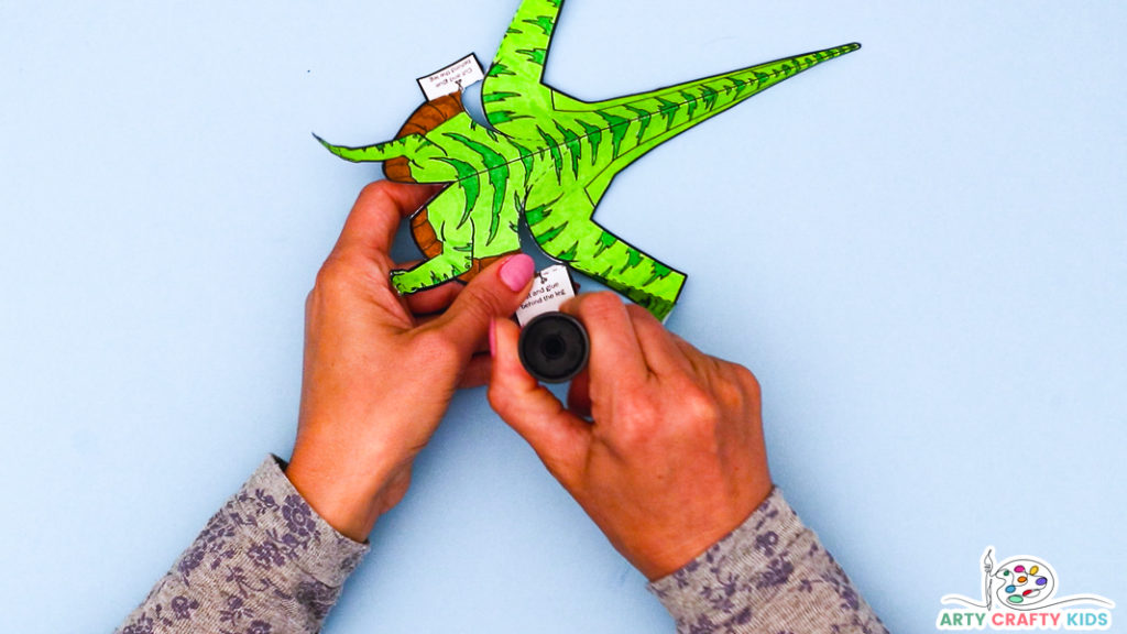 Image featuring a hand applying glue to the folds of the dinosaur's underbelly.