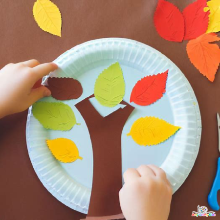 Image of a child's hand arranging Paper Autumn leaves around the tree branch.