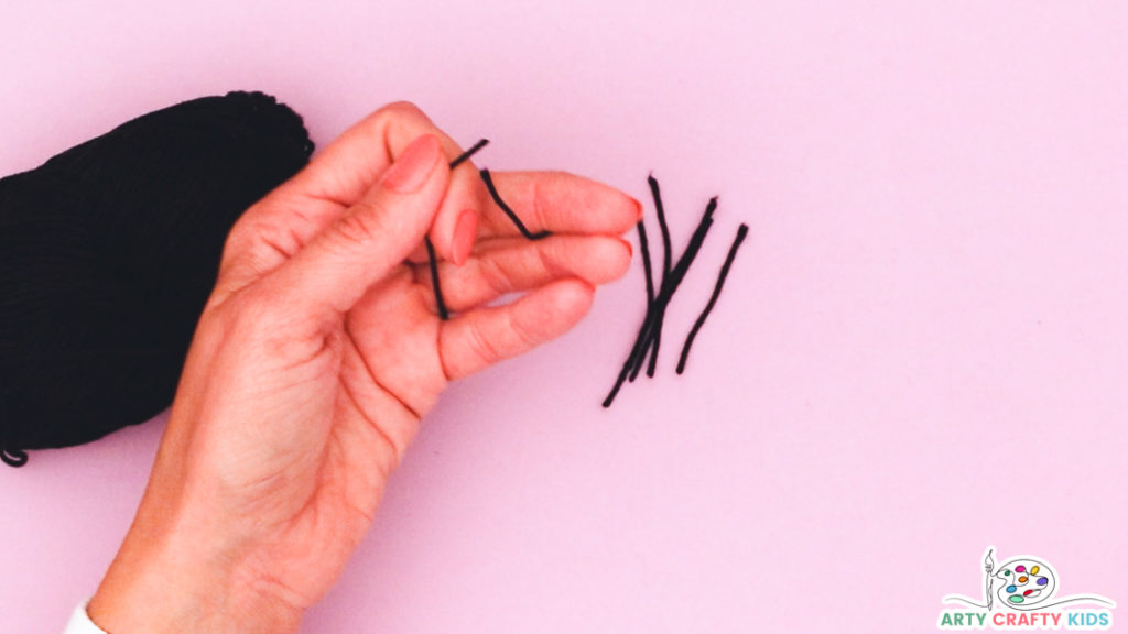Image of a hand showing multiple evenly cut pieces of black yarn for whiskers.