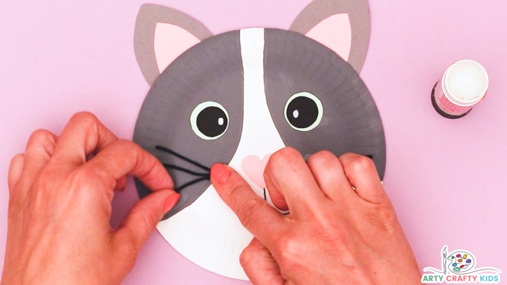 Image of a hand glueing the black whiskers onto the paper plate.