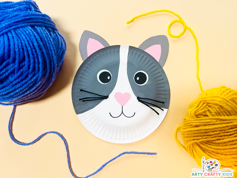 Image of a completed paper plate cat craft, surrounded by balls of yarn.