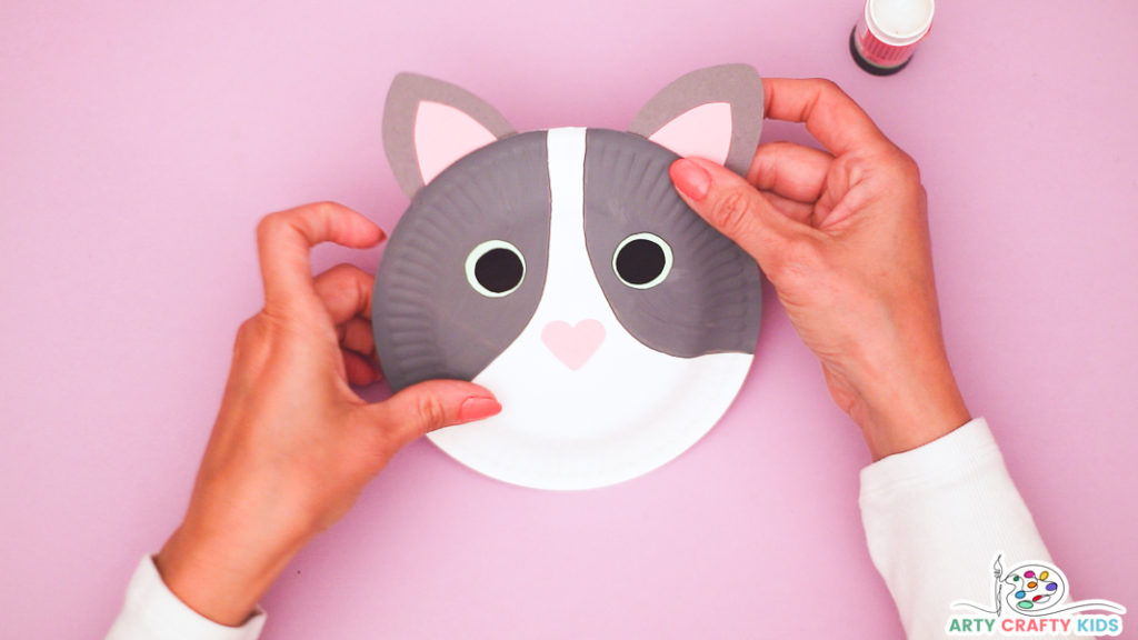 Image of a hand glueing the ears onto the paper plate cat.