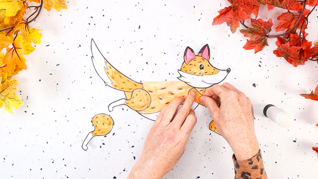 Image featuring a hand glueing the front and back legs onto the fox's body.