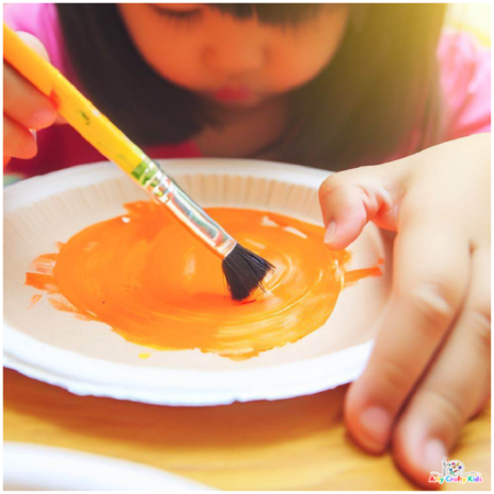 image of a child painting a paper plate orange.