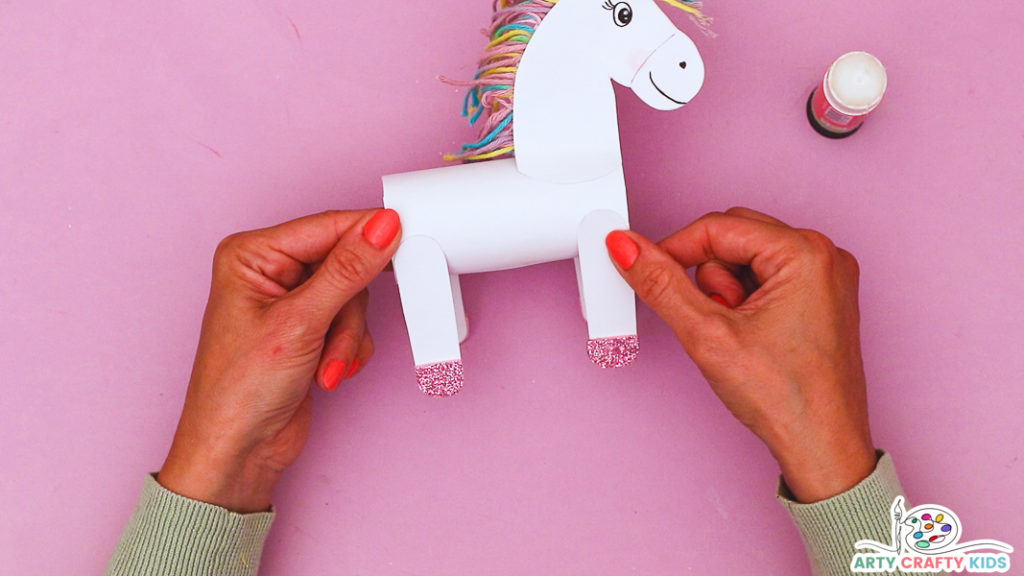 Image featuring a hand glueing 4 legs onto the unicorns body.