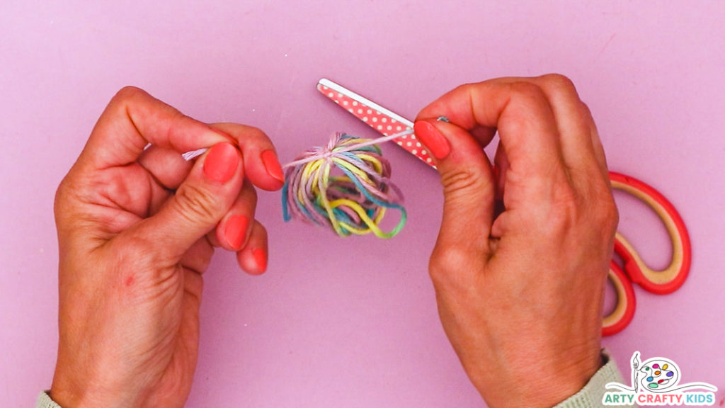 Image featuring a hand securing a circle of yarn with a thread of yarn.