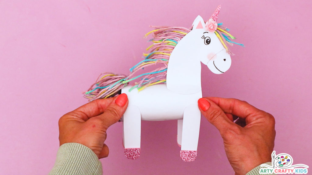 A pair of hands proudly holding a completed toilet paper roll unicorn craft.