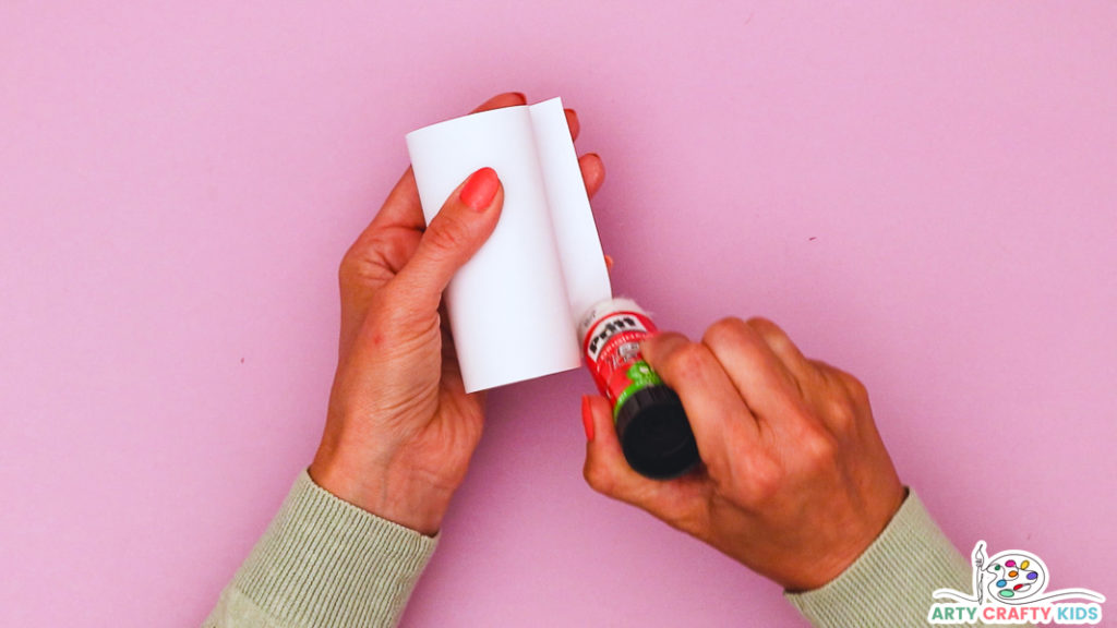 Image featuring a hand wrapping a piece of white paper around a toilet paper roll.