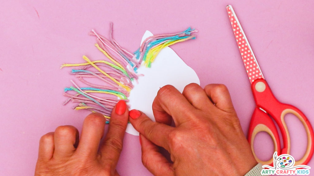 Image featuring a hand glueing yarn to the unicorn's head to create a rainbow colored mane.