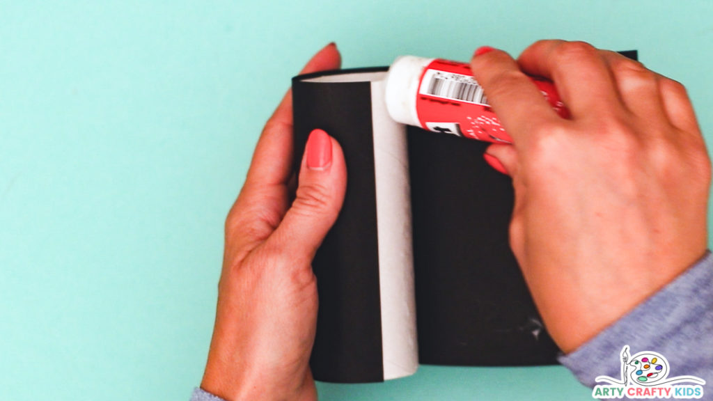 Image featuring a hand wrapping black paper around a paper roll.