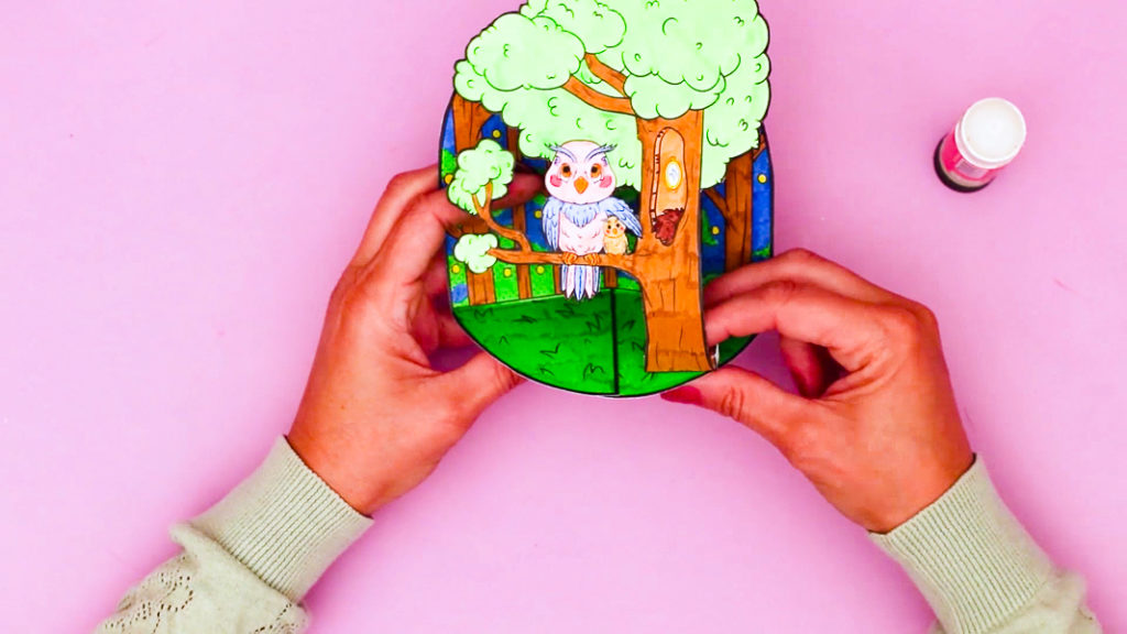 Image of a hand securing the pop-up owl to the grassy area of the woodland scene - completing the craft!
