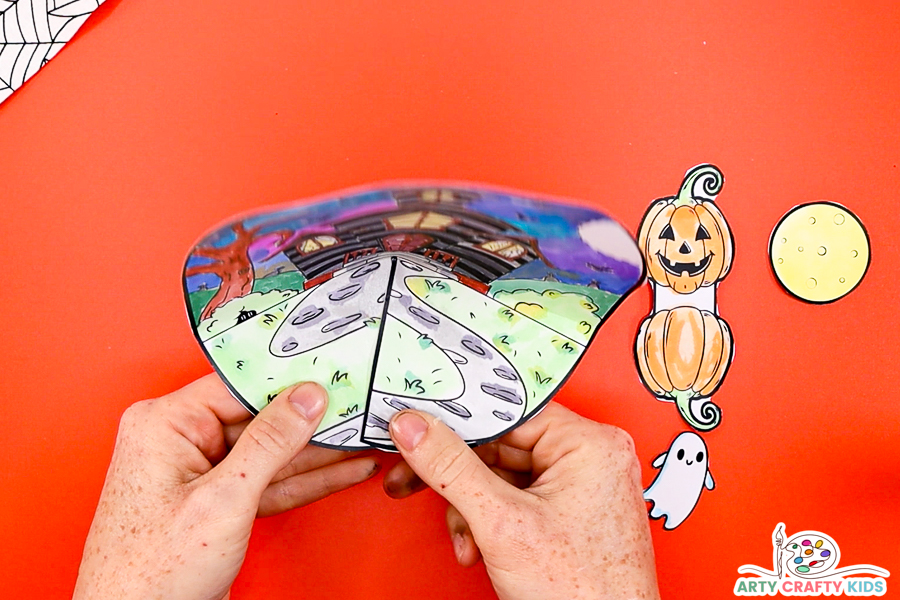 Step 4: Hands folding the tabs together to encourage the haunted house backdrop to pop. 