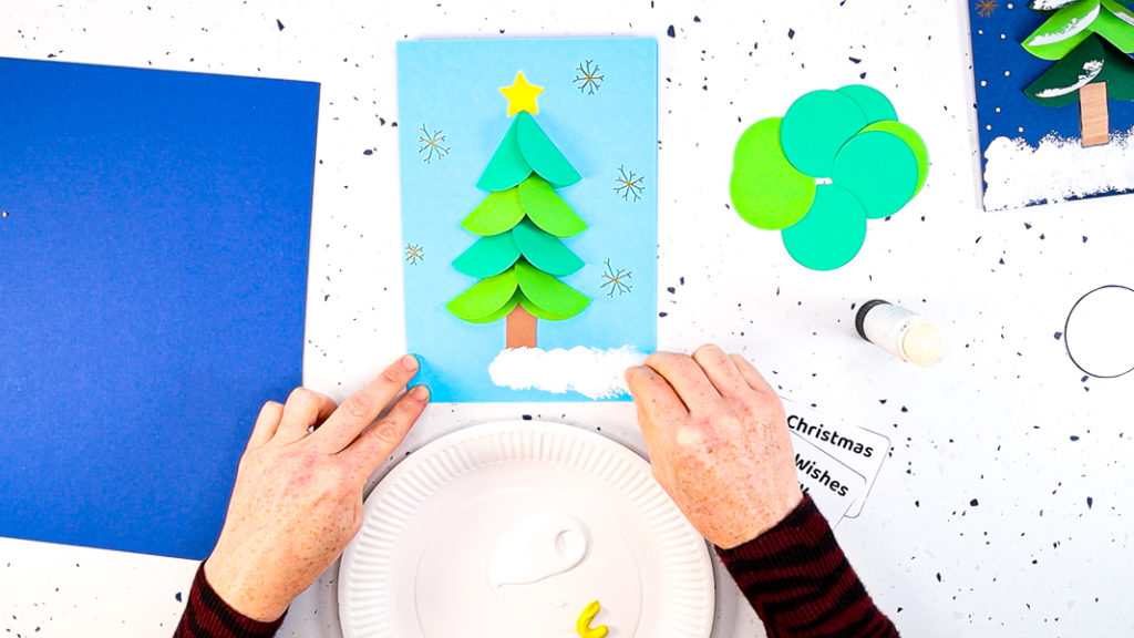 Hands using a pom-pom to print white paint along the bottom of the card.