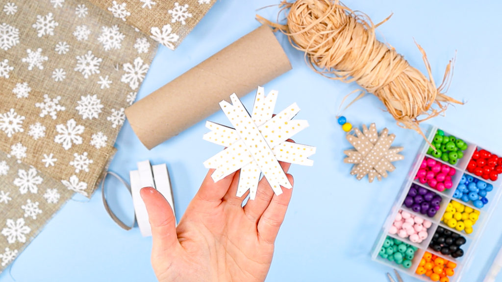 Image showing a hand holding a white paper roll snowflake with golden dots.