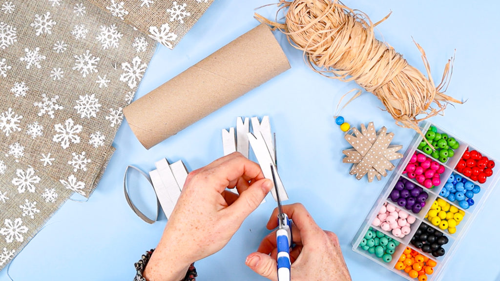 Image showing a hand cutting little triangular shapes out of the end of each paper roll snowflake piece.