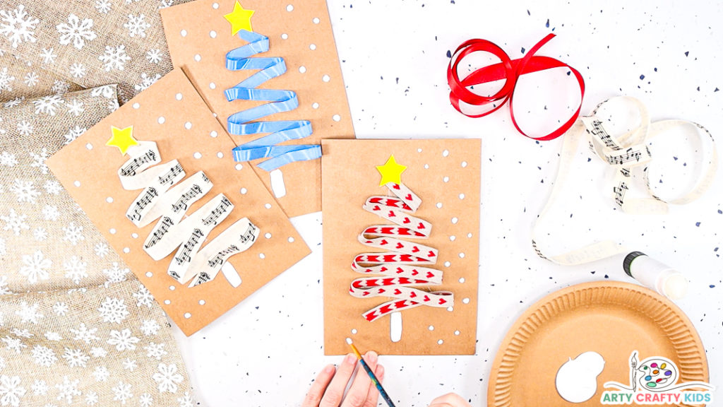 Image showing a hand painting white dots around the Christmas tree to convey snowfall.