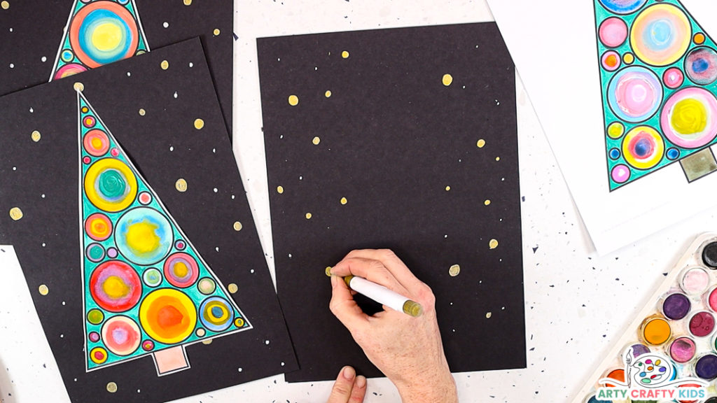 Image of a hand decorating a sheet of black card stock with metallic pens.