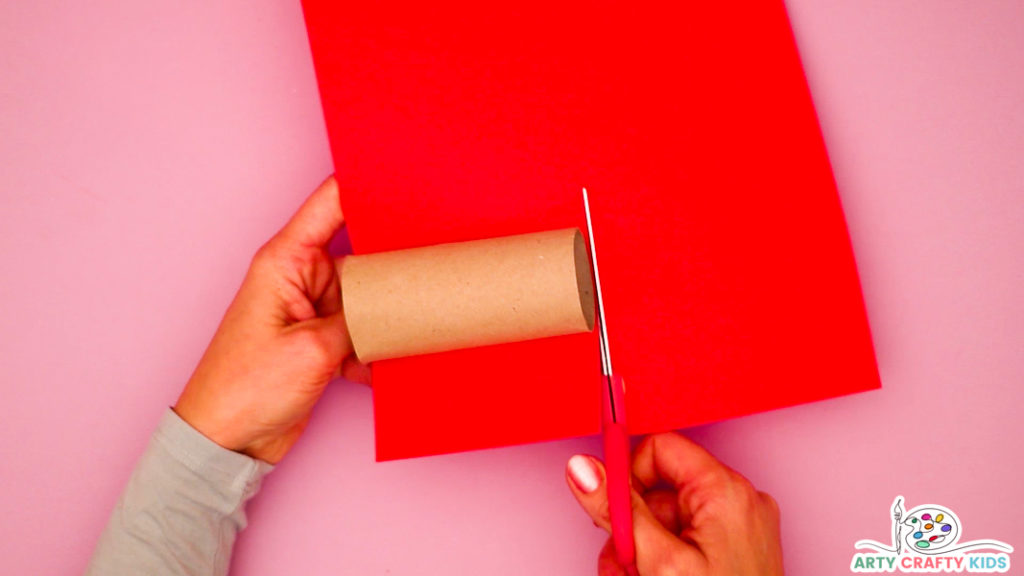 Step 1 - Image of a hand cutting red paper to size to wrap around a paper roll.