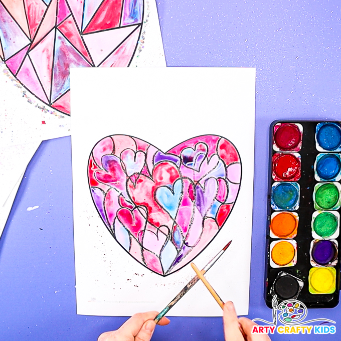 Image of a hand splattering watercolor paint around the outside of the painted geometric heart art.