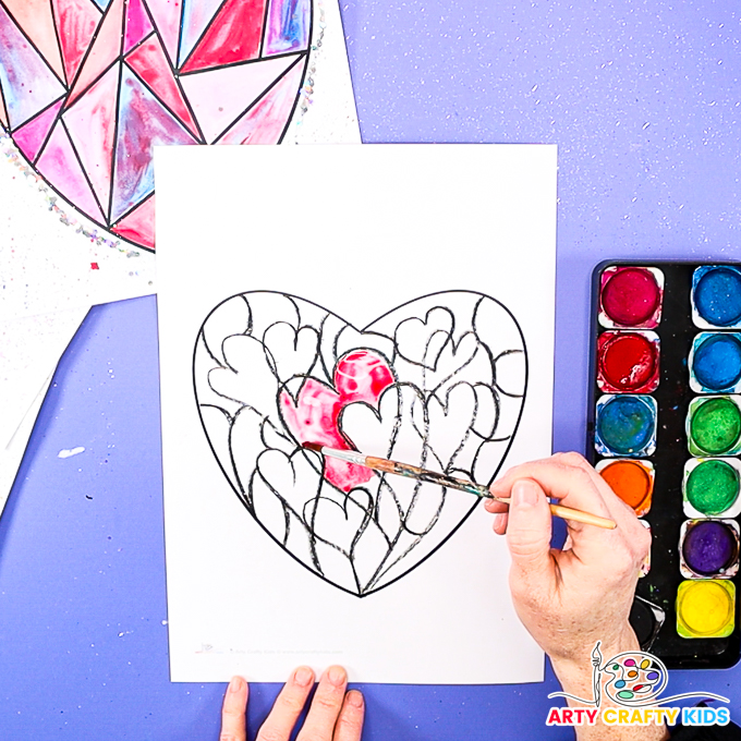 Image of a hand painting one of the segments within the hearts with watercolor paint.