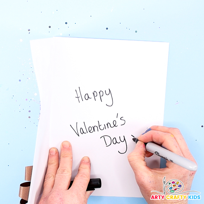 Image of a hand writing Happy Valentine's Day into the handprint valentine card.