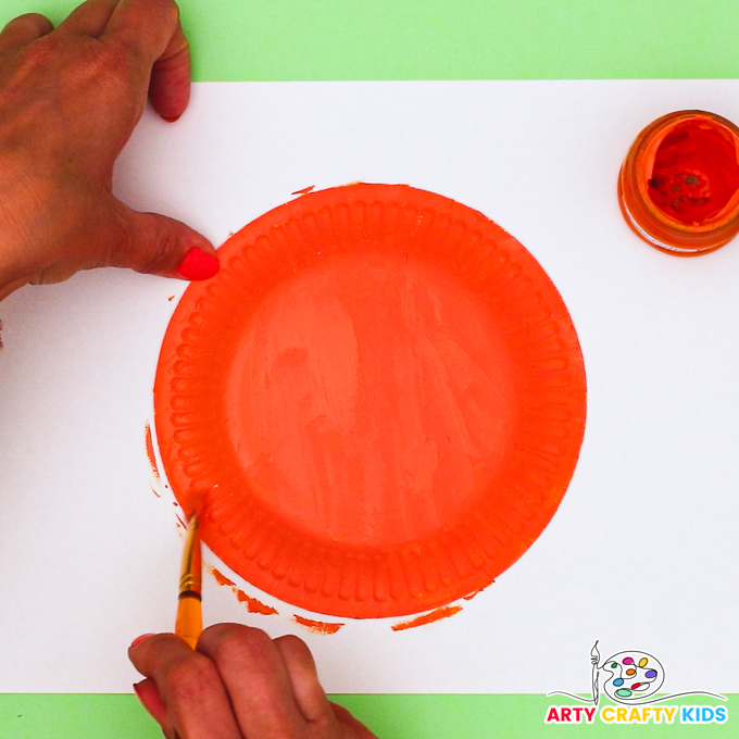 Image features a hand painting a paper plate orange.