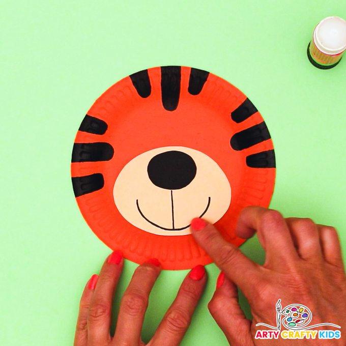 Image featuring a hand sticking the muzzle onto the paper plate tiger.