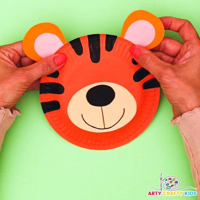 Image featuring a hand glueing the ears onto the paper plate tiger.