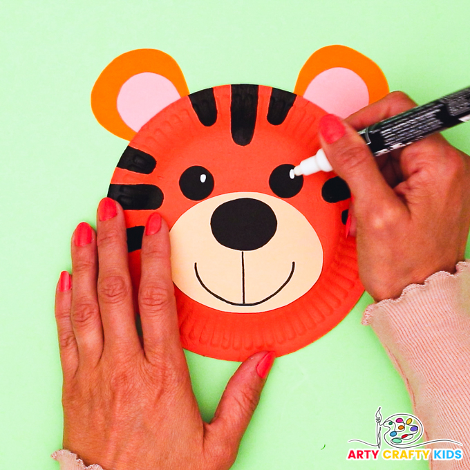 Image of hand drawing eyes onto the paper plate tiger craft.