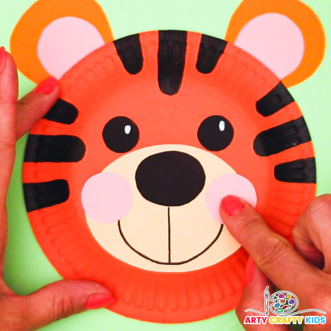 Image of a hand glueing a pair of pink cheeks onto the tiger.