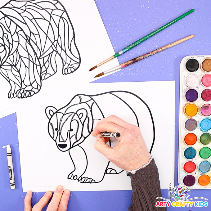 Image of a hand drawing lines with a black crayon to create abstract line art within the head segment of the polar bear template.